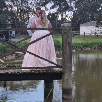 Bride and groom standing on a hedge by the water during an outdoor wedding photoshoot